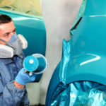 Student painting car exterior using tools and wearing protective gear