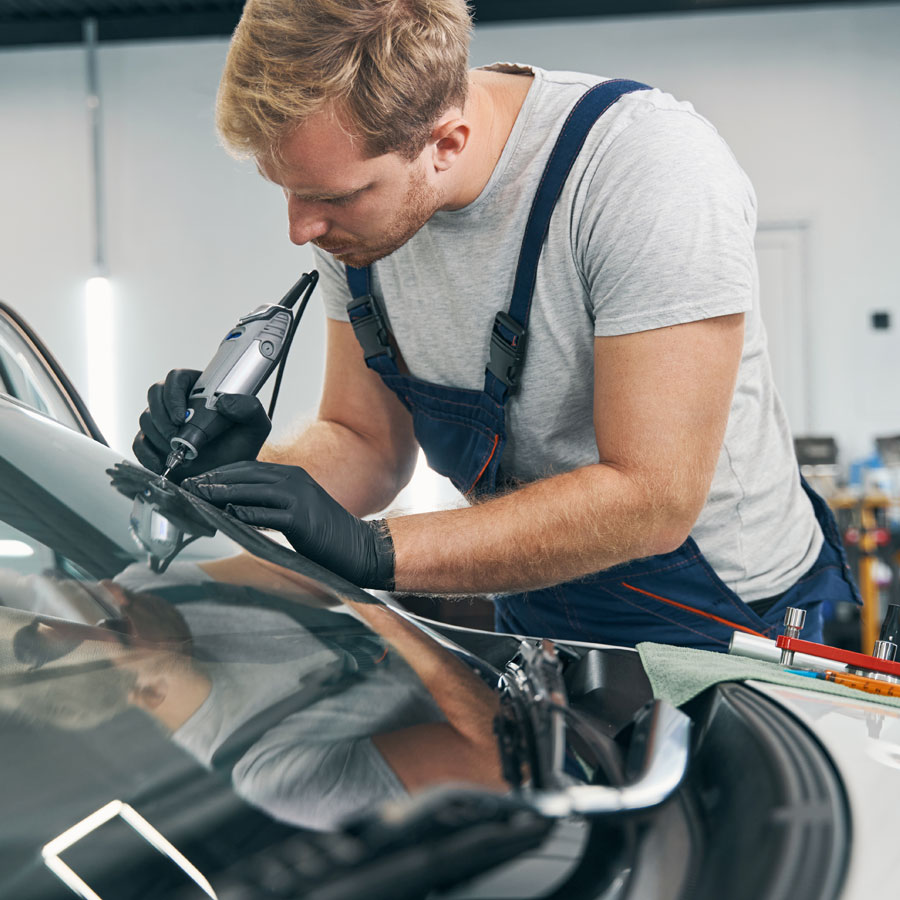 Auto repair technician working on car glass with tool